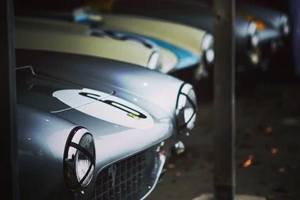 Row of vintage cars parked indoors with visible headlights and grilles.