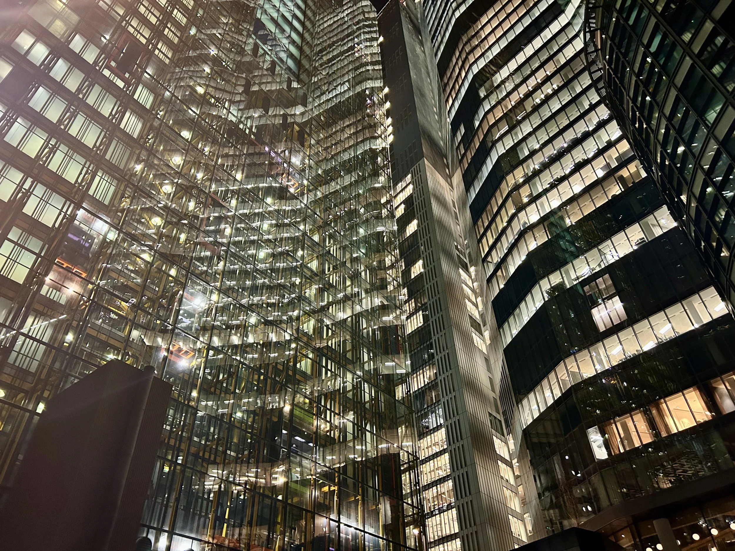 Night view of a modern glass skyscraper with illuminated office lights visible through the glass windows.