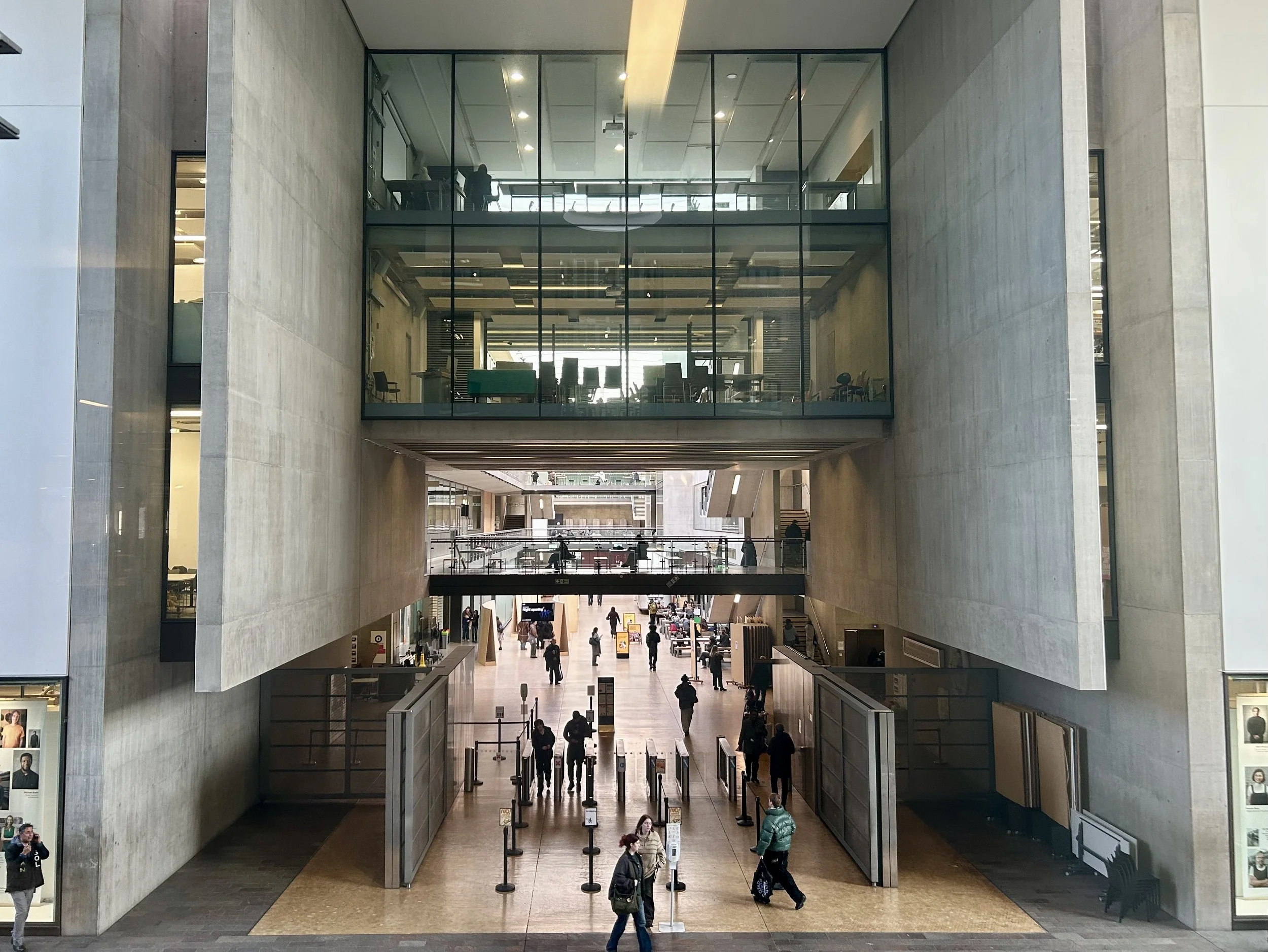 Interior view of a modern, multi-level airport or train station with high ceilings, large glass windows, and people walking through the main hall.