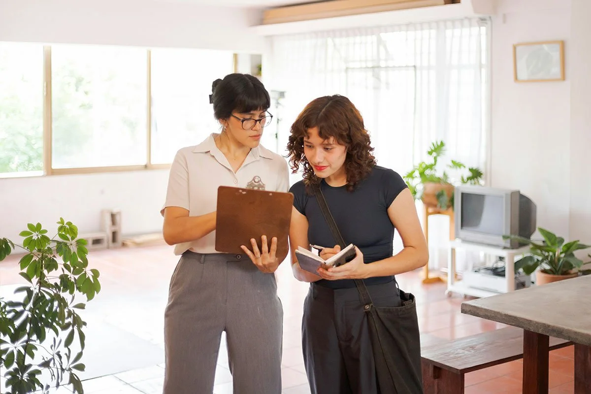 Deux femmes discutent et examinent des notes dans un salon lumineux.