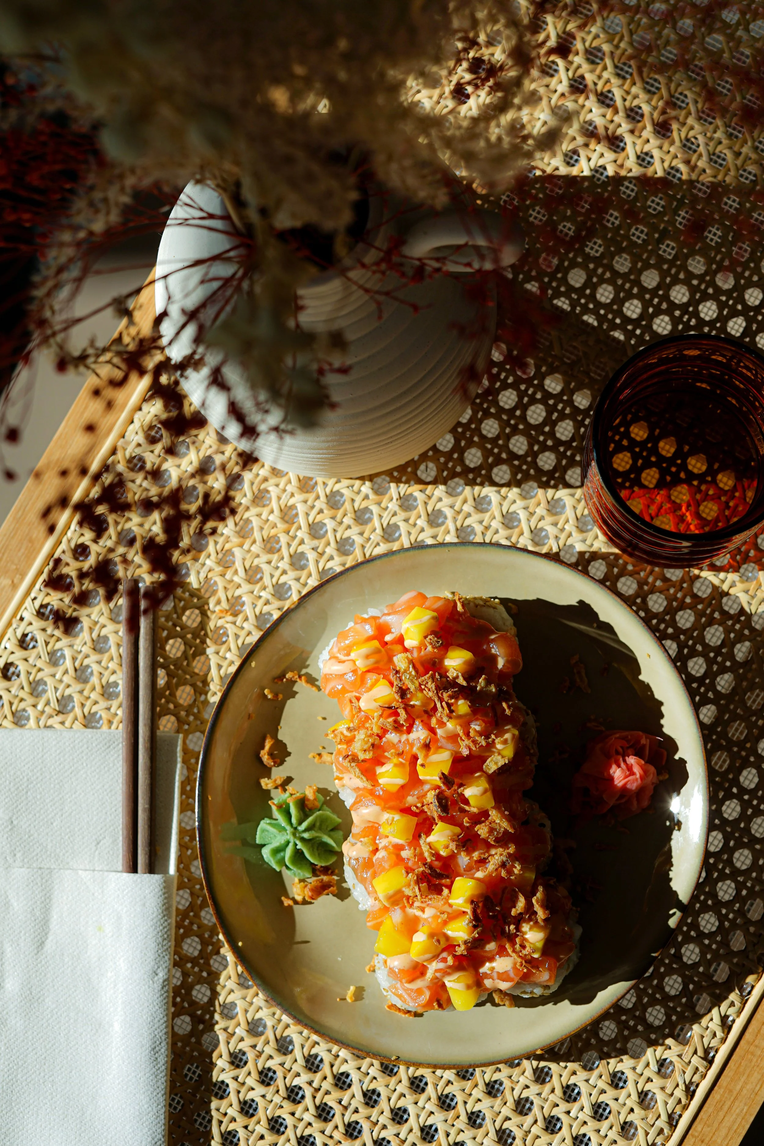 Plat de sushi avec du wasabi et du gingembre, un verre à boire, une nappe en bois et un set de table en rotin