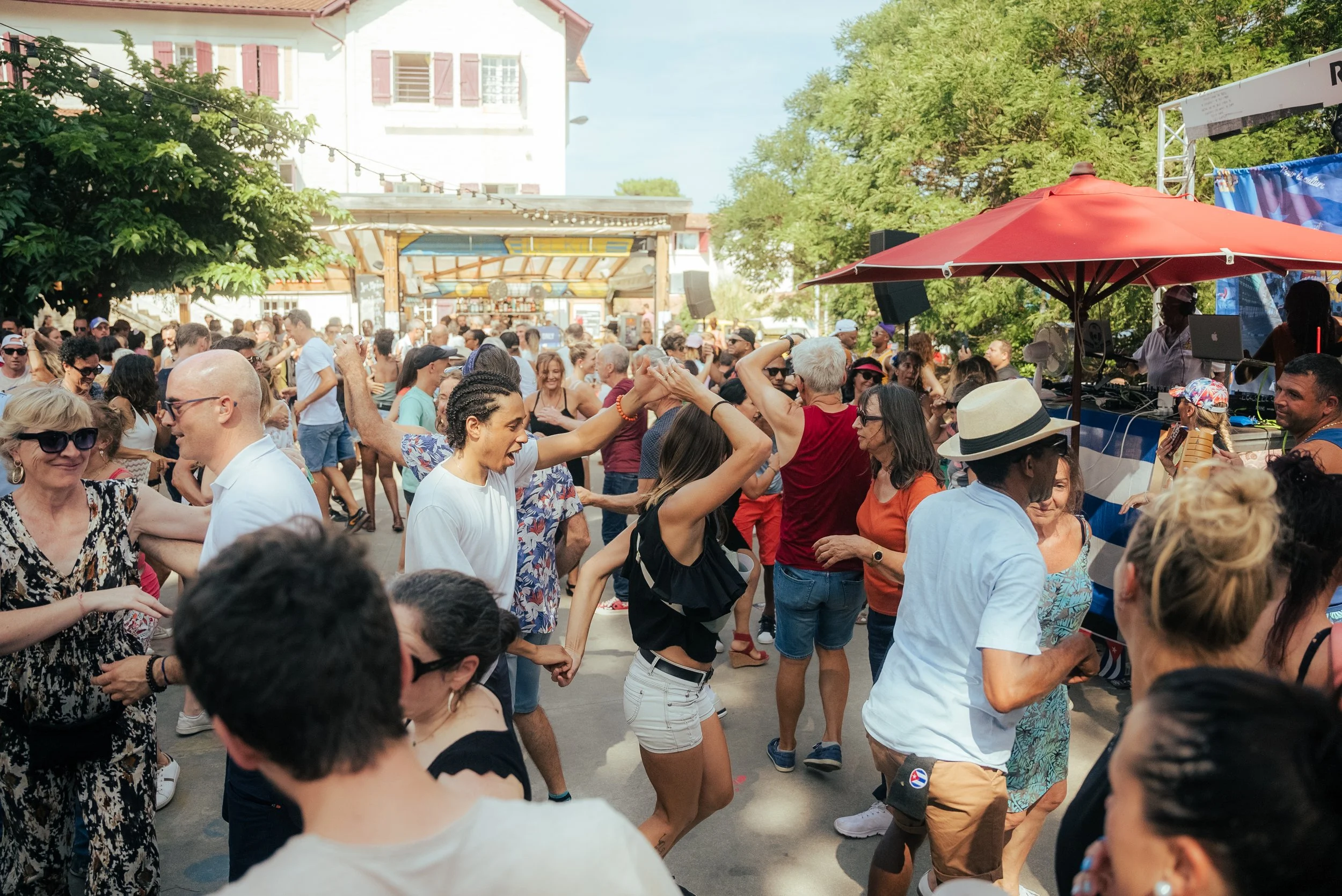 Groupe de personnes dansant lors d'une fête en plein air avec arbres et structure en arrière-plan.