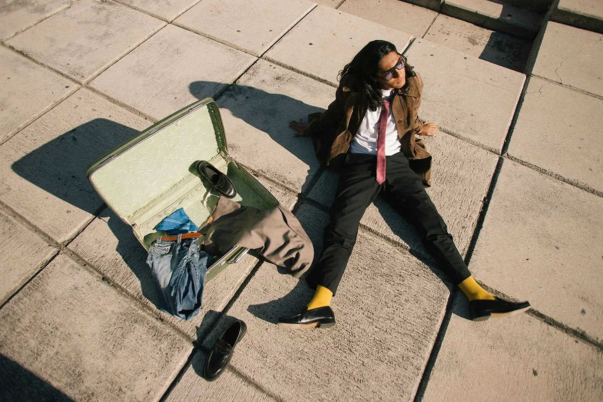 Une femme assise sur le trottoir avec une valise ouverte contenant des vêtements et des chaussures.