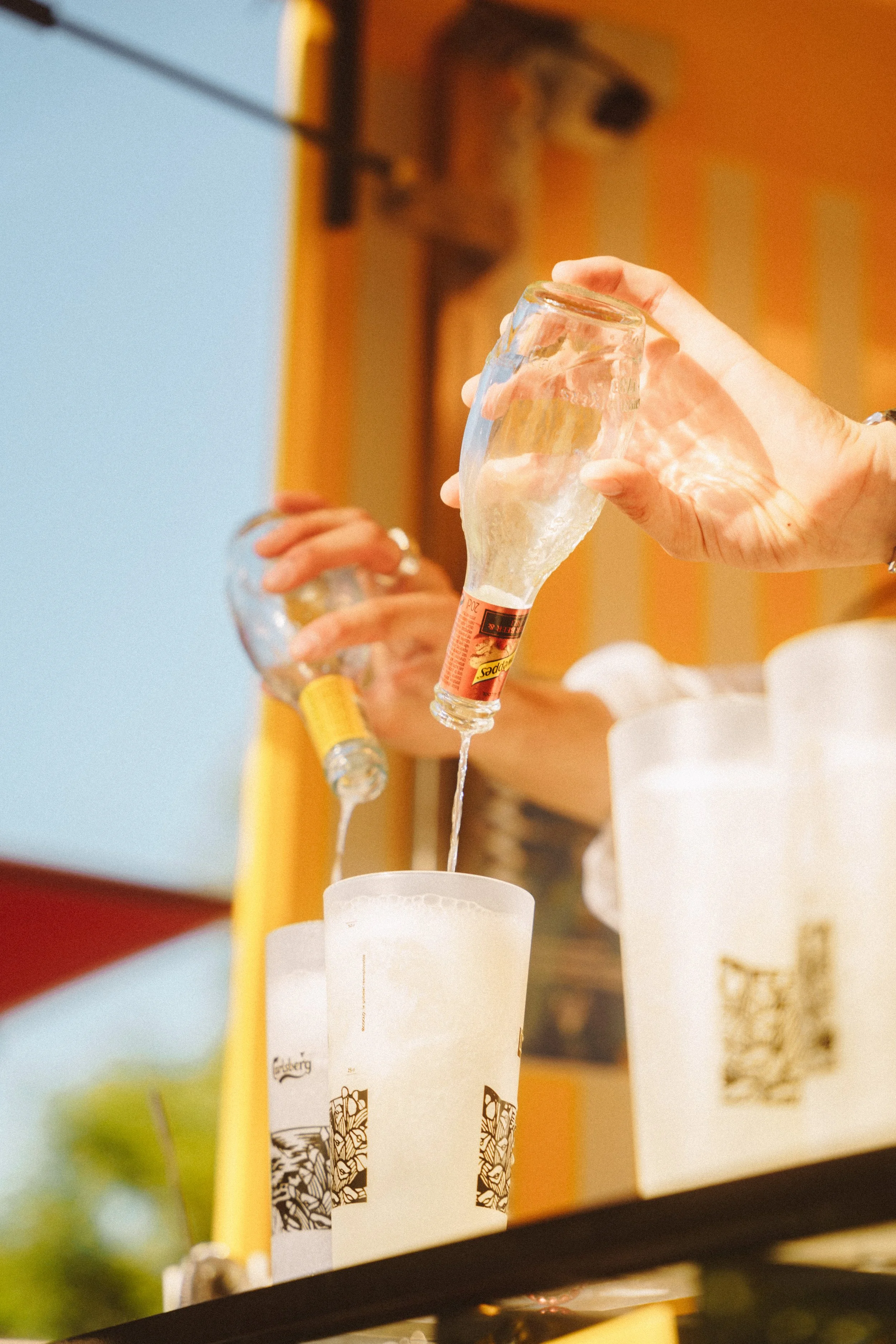 Une personne verse de la glace dans un grand verre à l'aide d'une bouteille. La scène se déroule probablement dans un café ou un restaurant.