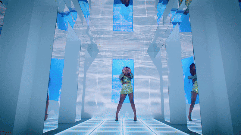 A gif of Drag Queen Mo Heart performing Miss Harlequin Toad, in a colourful dress in different settings - a futuristic, mirror-lined room with bright blue reflections, and rooms with images of the Harlequin Toad being projected onto the walls.