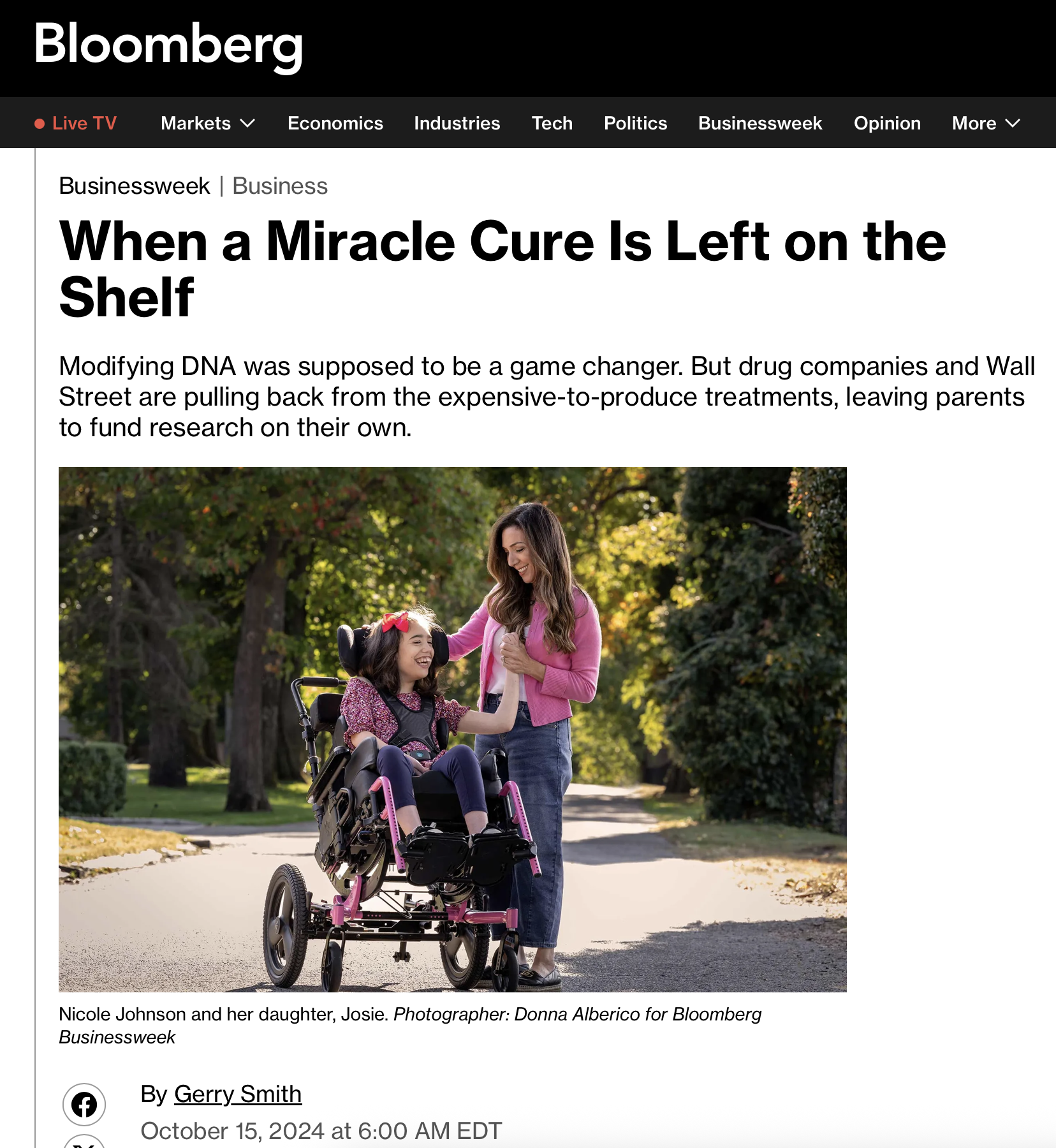 A woman in a pink jacket smiling and holding hands with a young girl in a wheelchair, outdoors in a park with trees and sunlight.