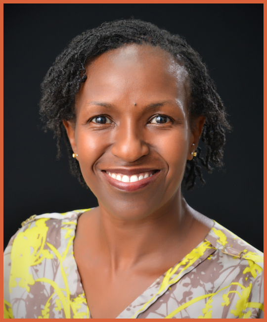 A smiling woman with short natural hair, earrings, wearing a yellow and gray patterned blouse, against a dark background.