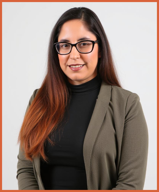 A woman with long brown hair and glasses, dressed in a black turtleneck and olive green blazer, smiling at the camera against a plain white background.