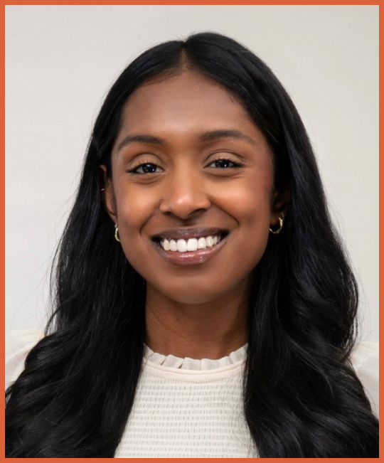 A young Black woman with long black hair, smiling, wearing a cream-colored top and small hoop earrings.