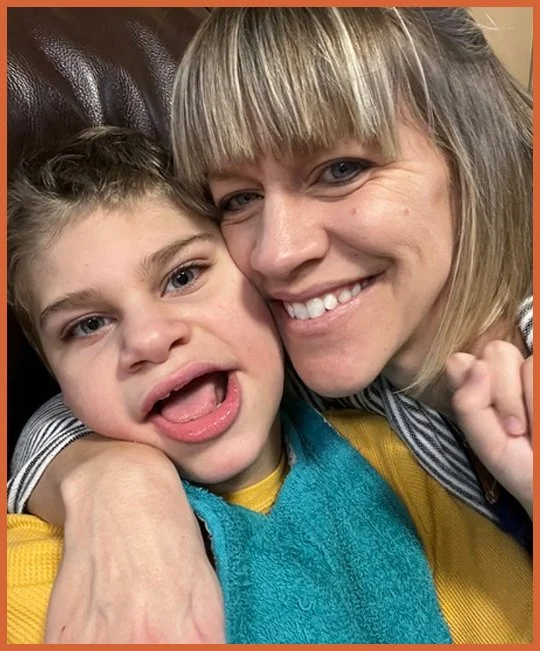 A woman and young boy smiling and cuddling together, sitting on a brown leather couch.