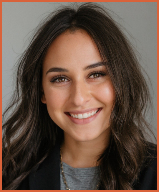 Close-up of a young woman with long dark hair, smiling, wearing a gray shirt and black blazer.