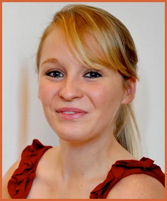 A young woman with blonde hair and blue eyes, wearing a red sleeveless top, smiling softly against a plain background.