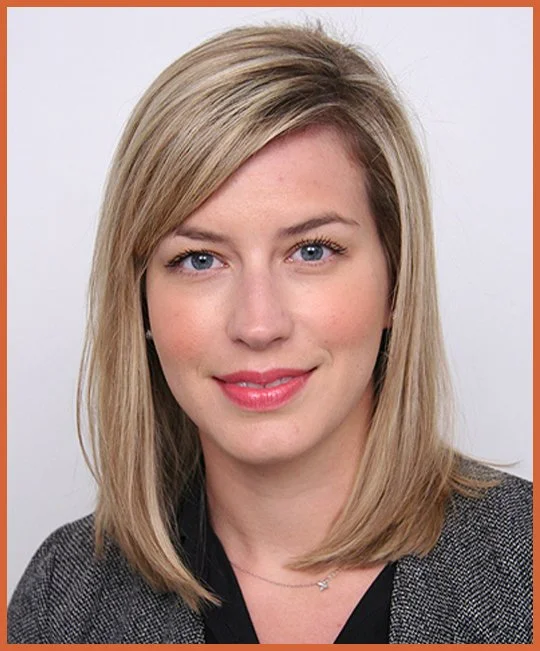 Headshot of a young woman with blonde hair, blue eyes, wearing a gray blazer and a black top, smiling at the camera against a white background with an orange border.
