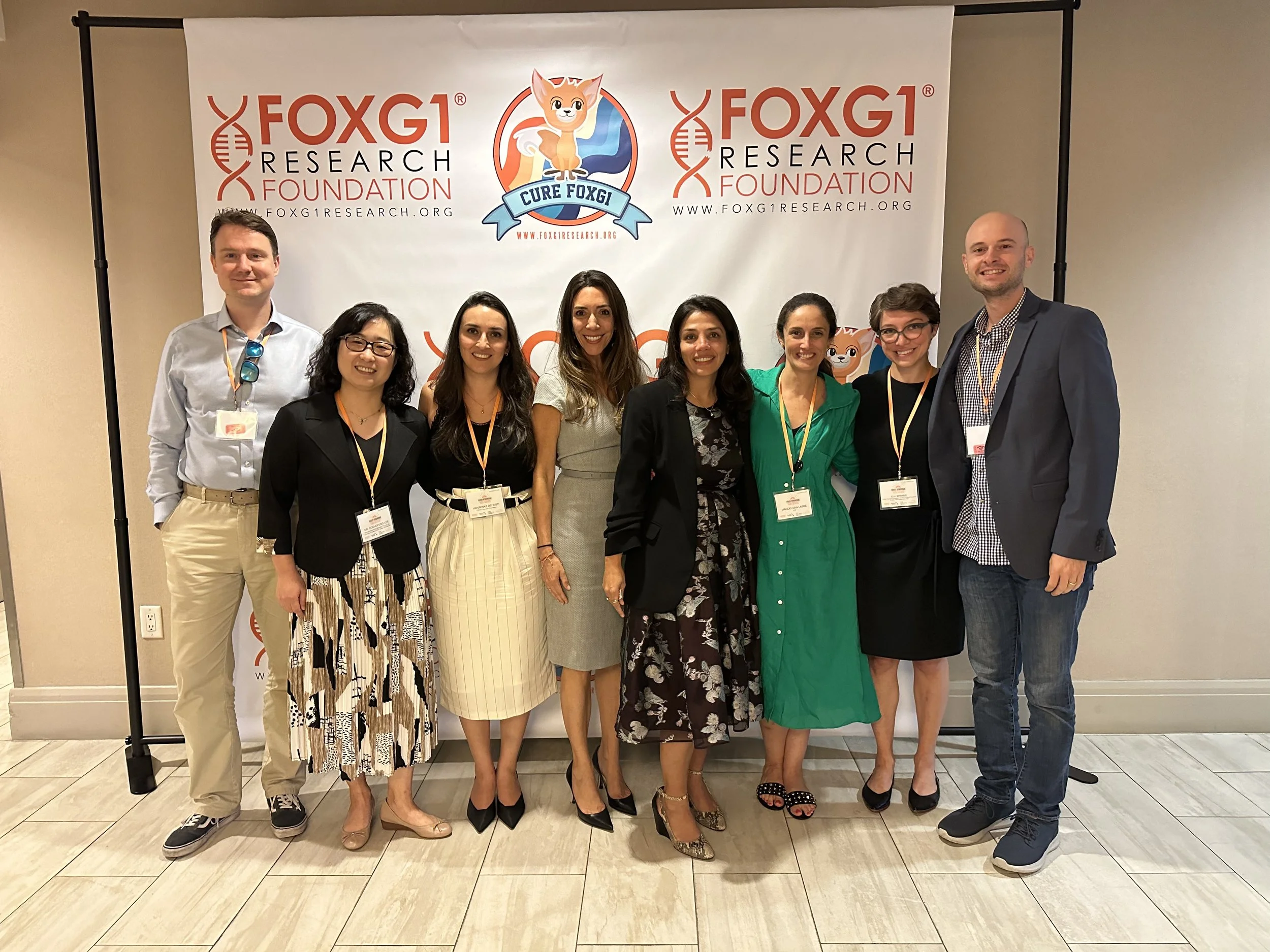 Group of nine people standing in front of a FOXG1 Foundation banner at an event, smiling and posing for the photo.