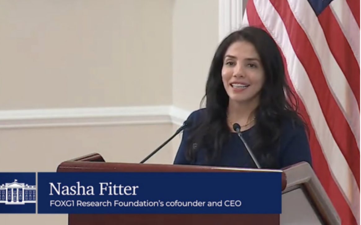 Image of Nasha Fitter from FOXG1 Research Foundation speaking at a podium at the White House with an American flag in the background. The text on the screen identifies her as Nasha Fitter, FOX61 Research Foundation's cofounder and CEO.