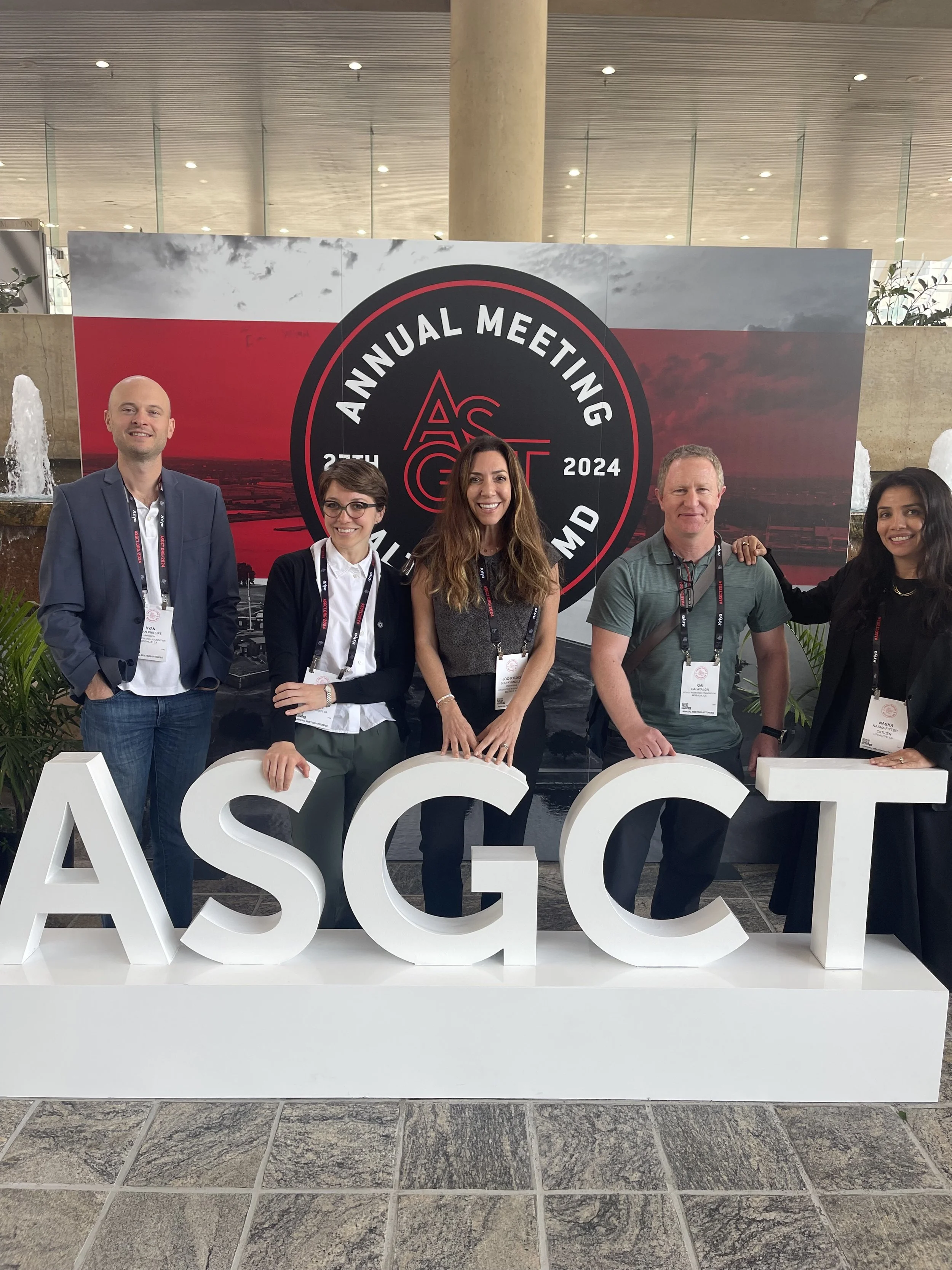 Group of five people attending the ASGCT 2024 Annual Meeting in Maryland, standing in front of a large event sign with large white letters spelling 'ASGCT' and a backdrop with the event logo.