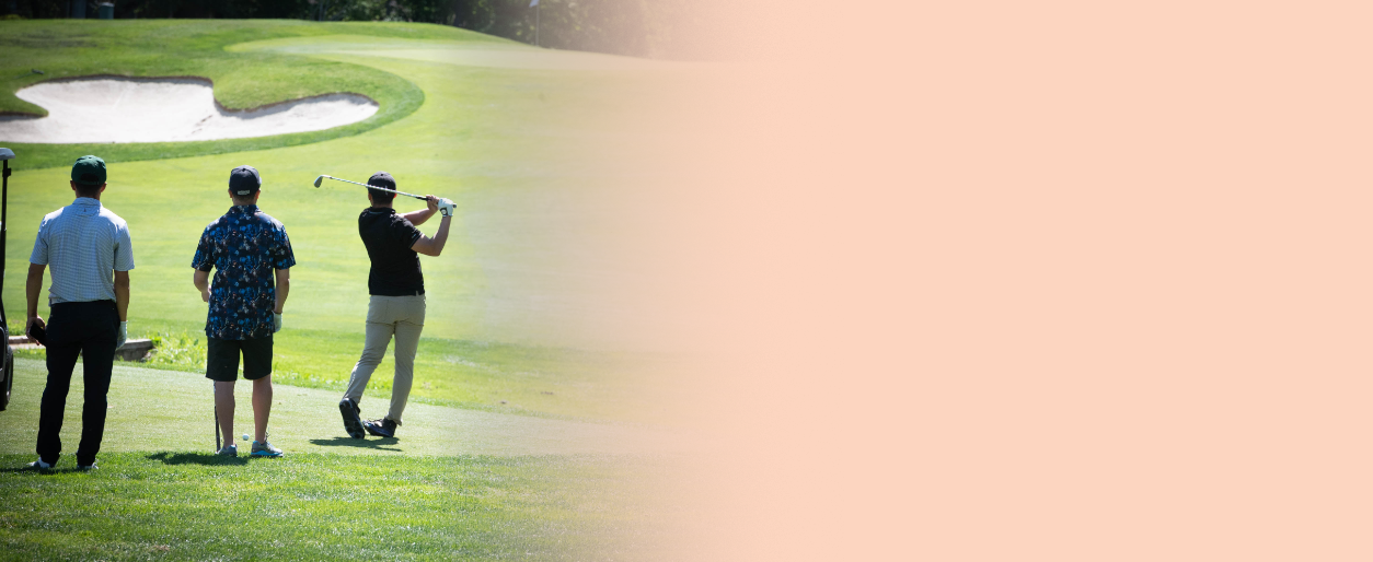 A golfer swinging a club on a golf course with two men watching, and sand traps nearby.