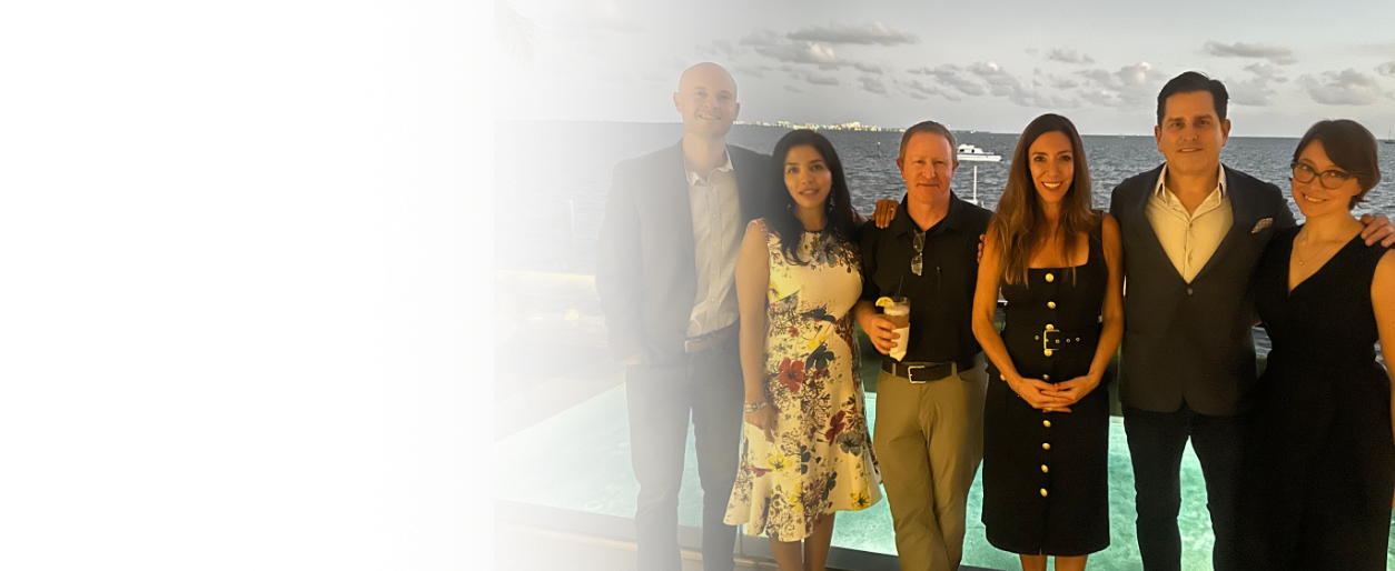 Group of six people standing together on a balcony with ocean view, smiling at the camera, during a social gathering.