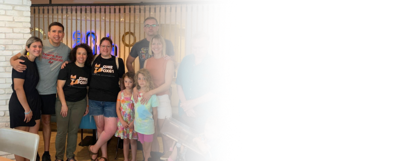 Group of people gathered together at an event inside a restaurant or cafe, with some children and adults smiling at the camera.