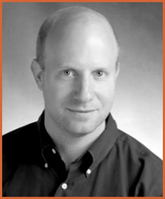 Black and white portrait of a man with short hair, wearing a collared shirt, smiling slightly, against a gradient background.