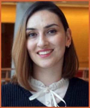 A woman with shoulder-length brown hair smiling indoors with a warm background.