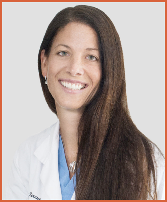 Professional portrait of a woman with long brown hair wearing a white medical coat and blue scrubs, smiling.