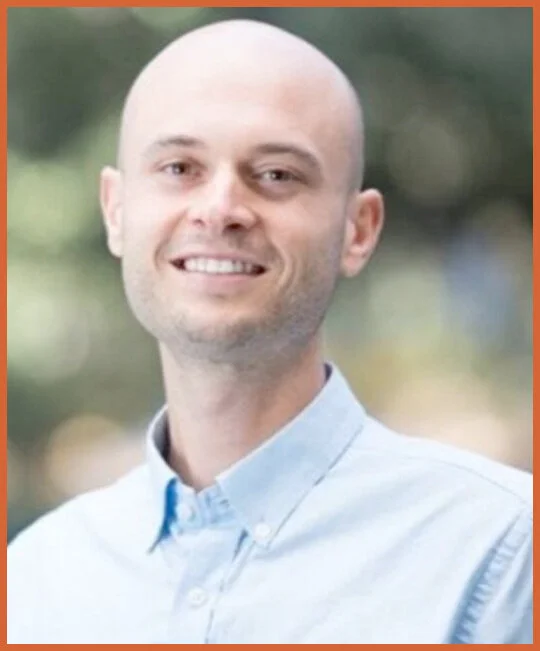 Image of Ryan Philips, CFO of the FOXG1 Research Foundation  in light blue button-up shirt smiling outdoors with blurred greenery background.