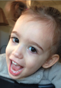 Close-up of a young girl with light skin and brown hair, smiling and showing her teeth