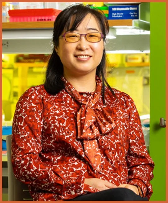 Image of Dr. Soo-Kyeung Lee, FOXG1 scientists and mom wearing glasses and black hair smiling in a lab or store, wearing a red patterned blouse.