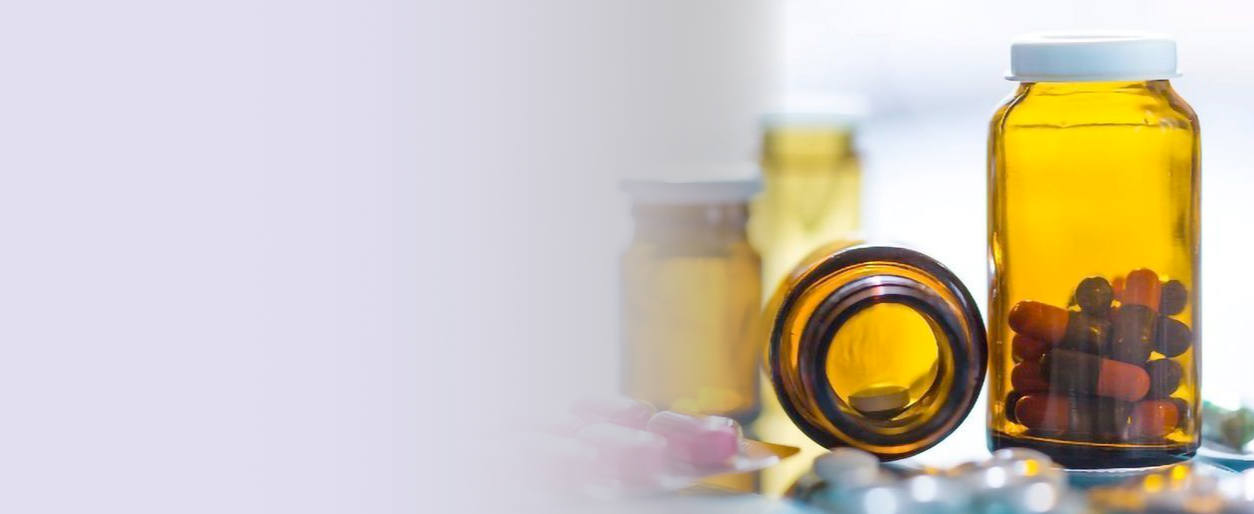 Two amber pill bottles, one upright and one on its side, with various pills and capsules spilling out, set on a surface with additional bottles in the background.