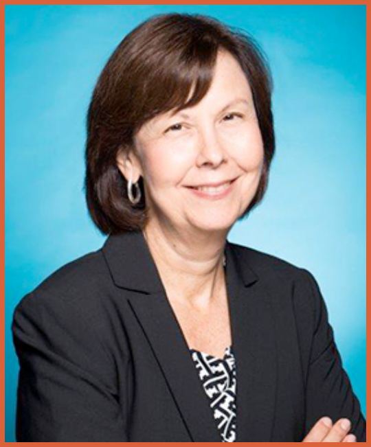 A middle-aged woman with dark brown hair, wearing a black blazer and hoop earrings, smiling against a blue background.