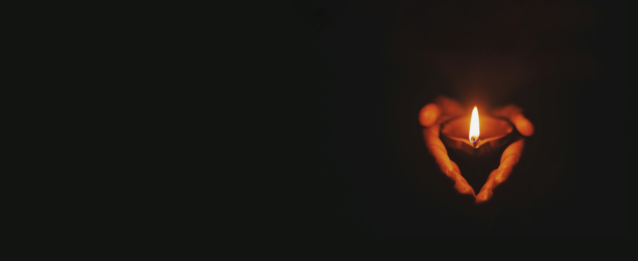 Person's hands cupping a lit candle against a dark background.