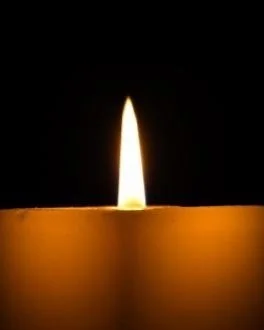 Close-up of a lit candle with a glowing flame in the dark.