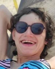 Woman with curly hair and sunglasses smiling outdoors