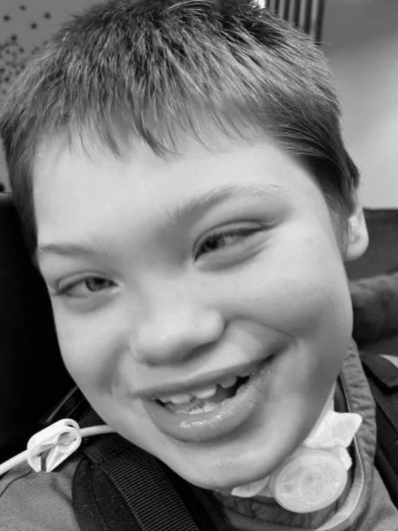 A smiling boy with short hair, wearing a neck brace and a backpack.