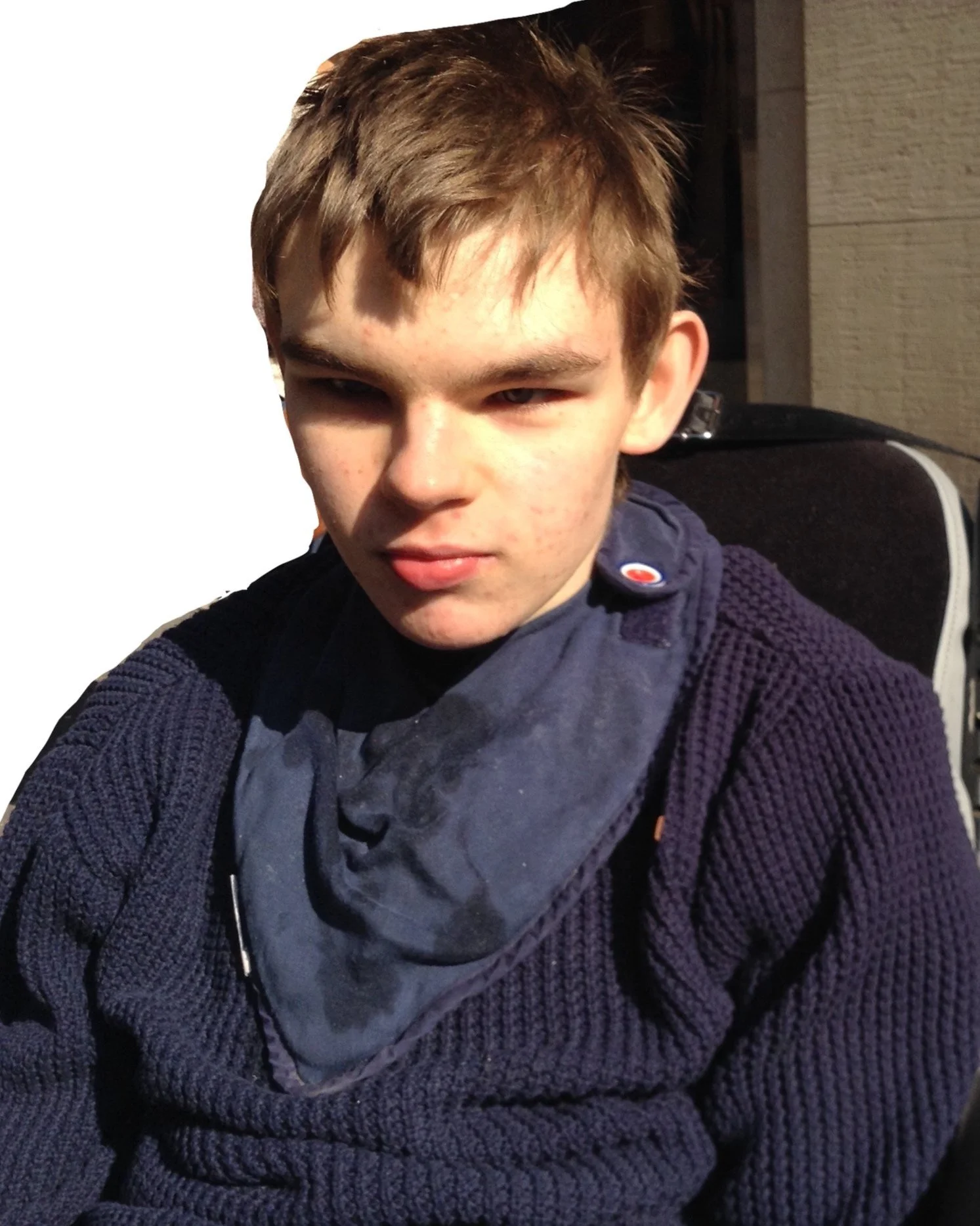 Young boy with light brown hair wearing a navy blue knit sweater and a gray scarf sitting outdoors at night.