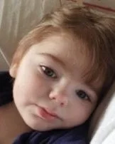 Close-up of a young child with reddish-brown hair resting their head on a pillow.