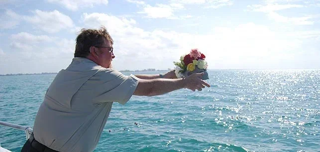 A man tossing flowers and an urn into the water for a memorial sail