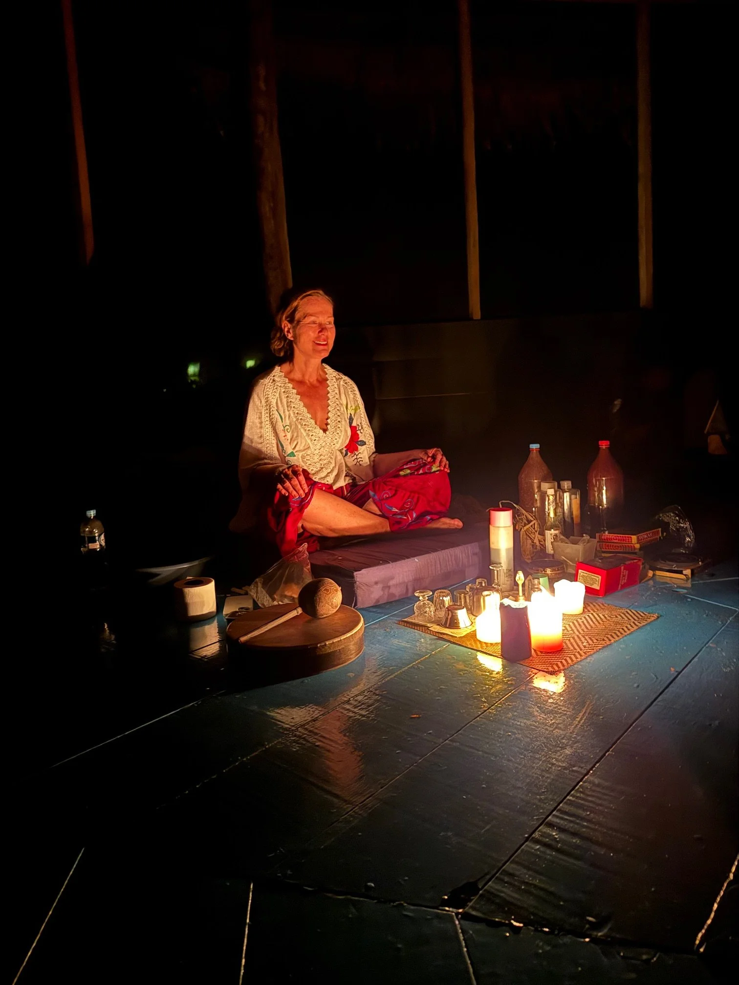 Monica Poshman sitter på golvet i Maloka i Peru, Amazonas omgiven av tända ljus, flaskor och olika föremål.