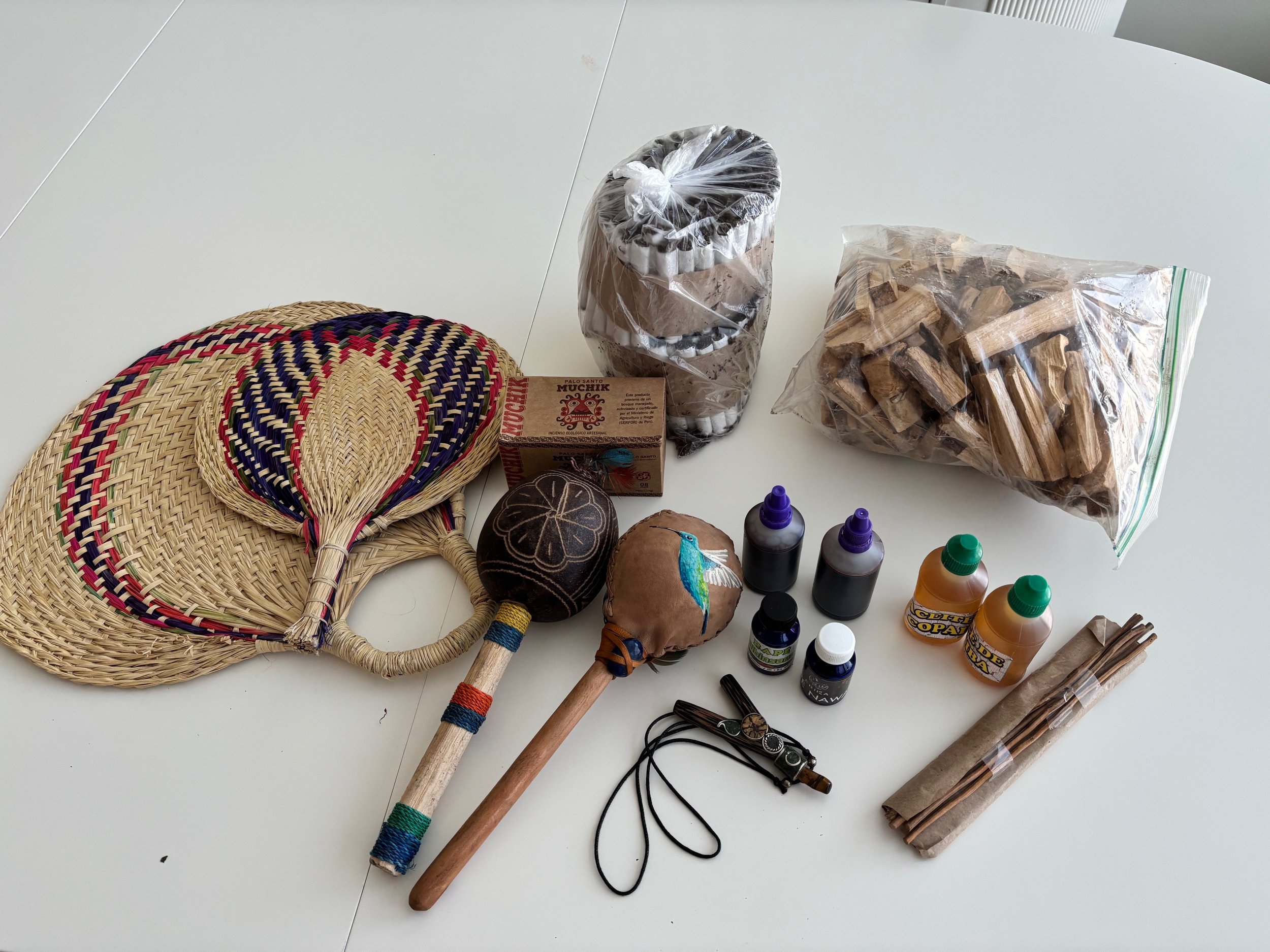 En bunt av olika hantverksmaterial och verktyg, inklusive flätade väskor, hantel, färgburkar, lim, tyg, samt en påse med träbitar och andra små föremål.