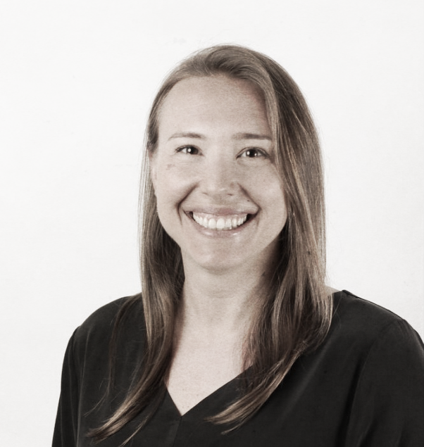 A smiling woman with long brown hair in a black top, standing against a plain white background.