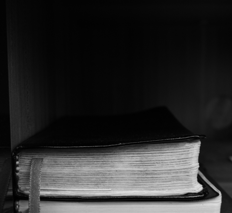 Close-up of a thick, hardcover book with a bookmark, on a wooden shelf.