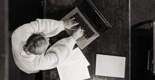 A person working at a desk using a laptop, with papers and a notebook on the desk.