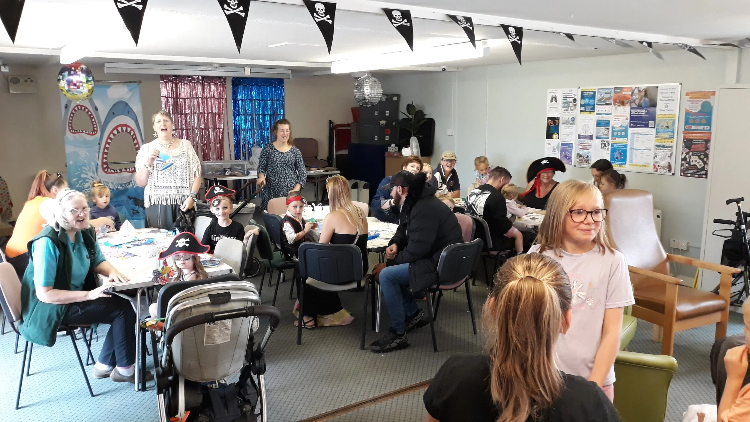 Four large cupcakes on a table, with three visible on white napkins and one partially visible on the left. Each cupcake has a small sign with a quote, including 'Move mountains with me,' 'This will hit the spot,' 'Step up to this plate,' and 'Because YUM.' A card at the bottom reads 'Supported By Villages Together'.