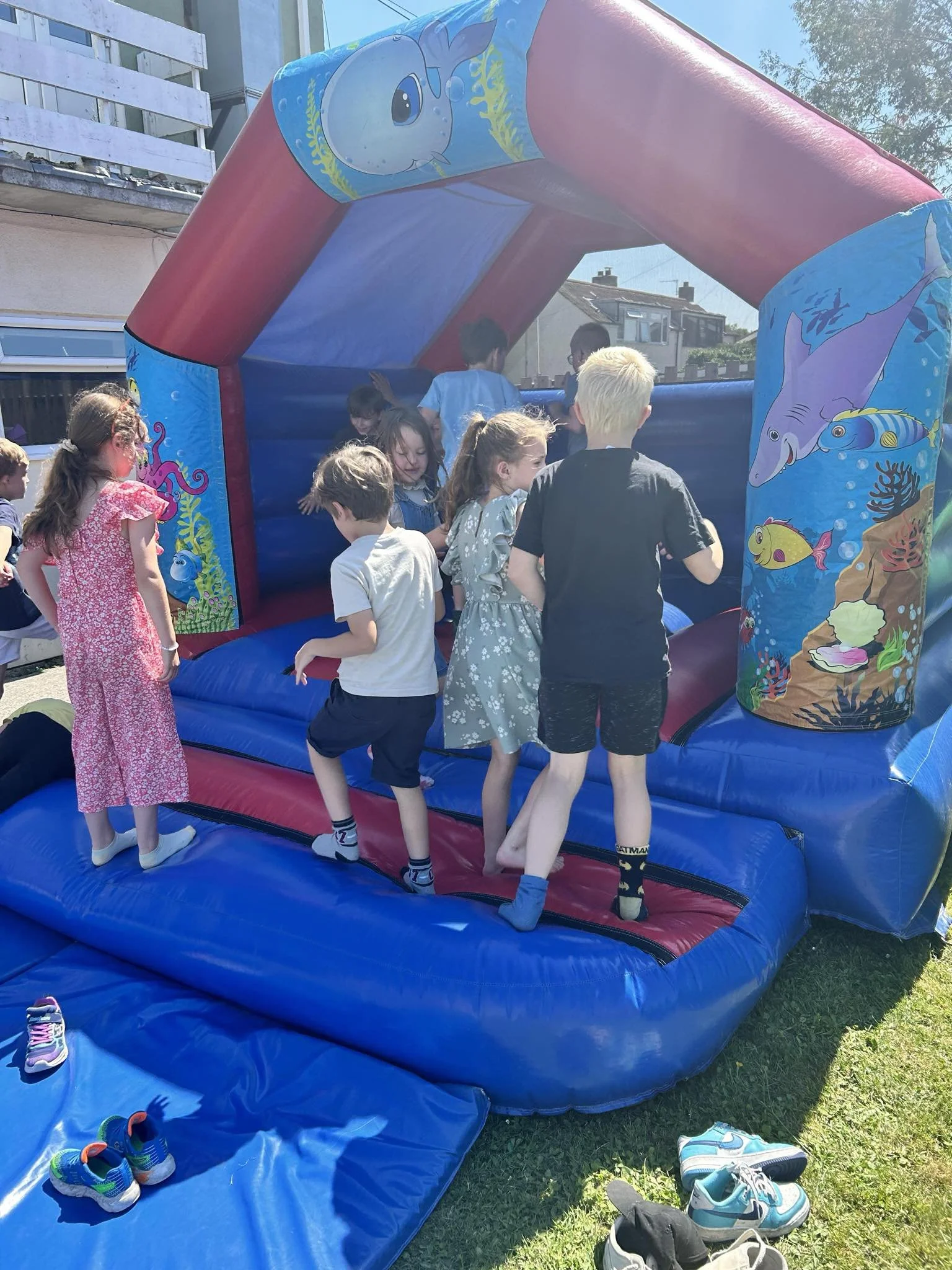 Children playing on an underwater-themed inflatable bounce house outdoors on a sunny day.