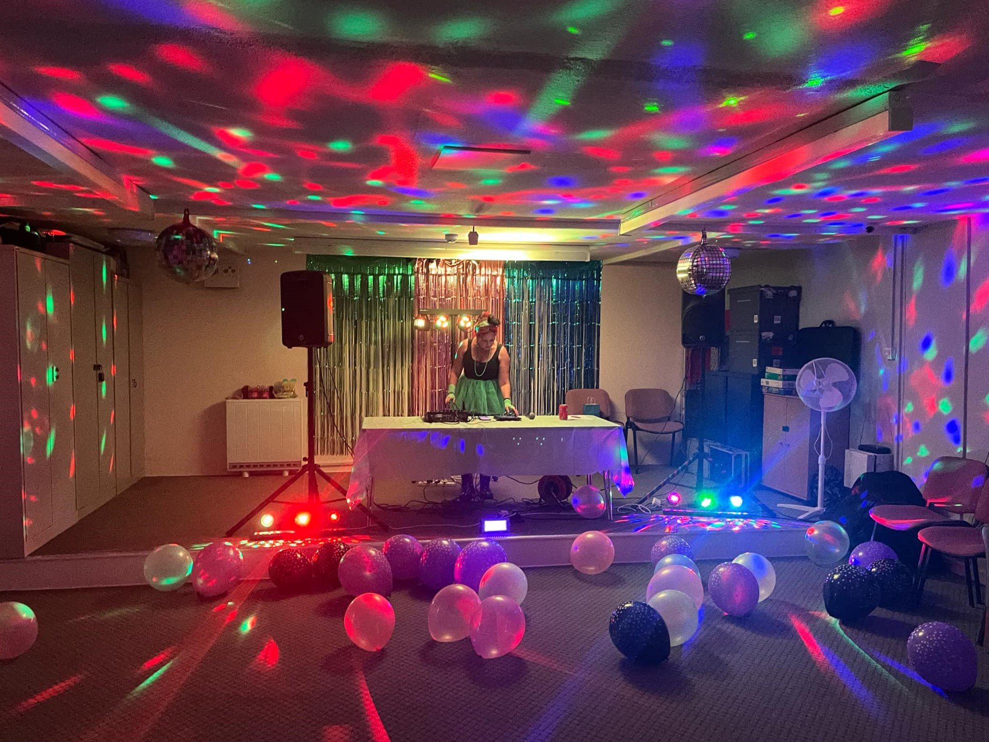 Two men smiling and talking in front of banners at a community event, one in a black shirt with a badge, the other with a beard and black shirt.
