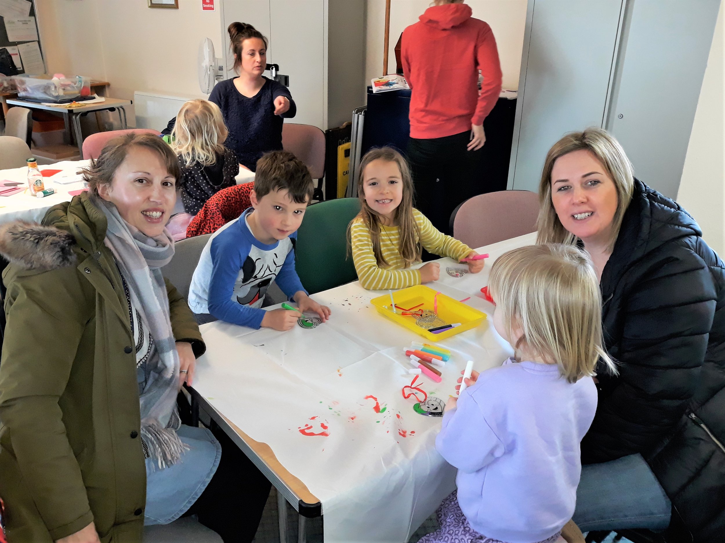 Children dancing, playing, and sitting in a dimly lit party room decorated with balloons and colorful disco lights, with a small stage area at the front.