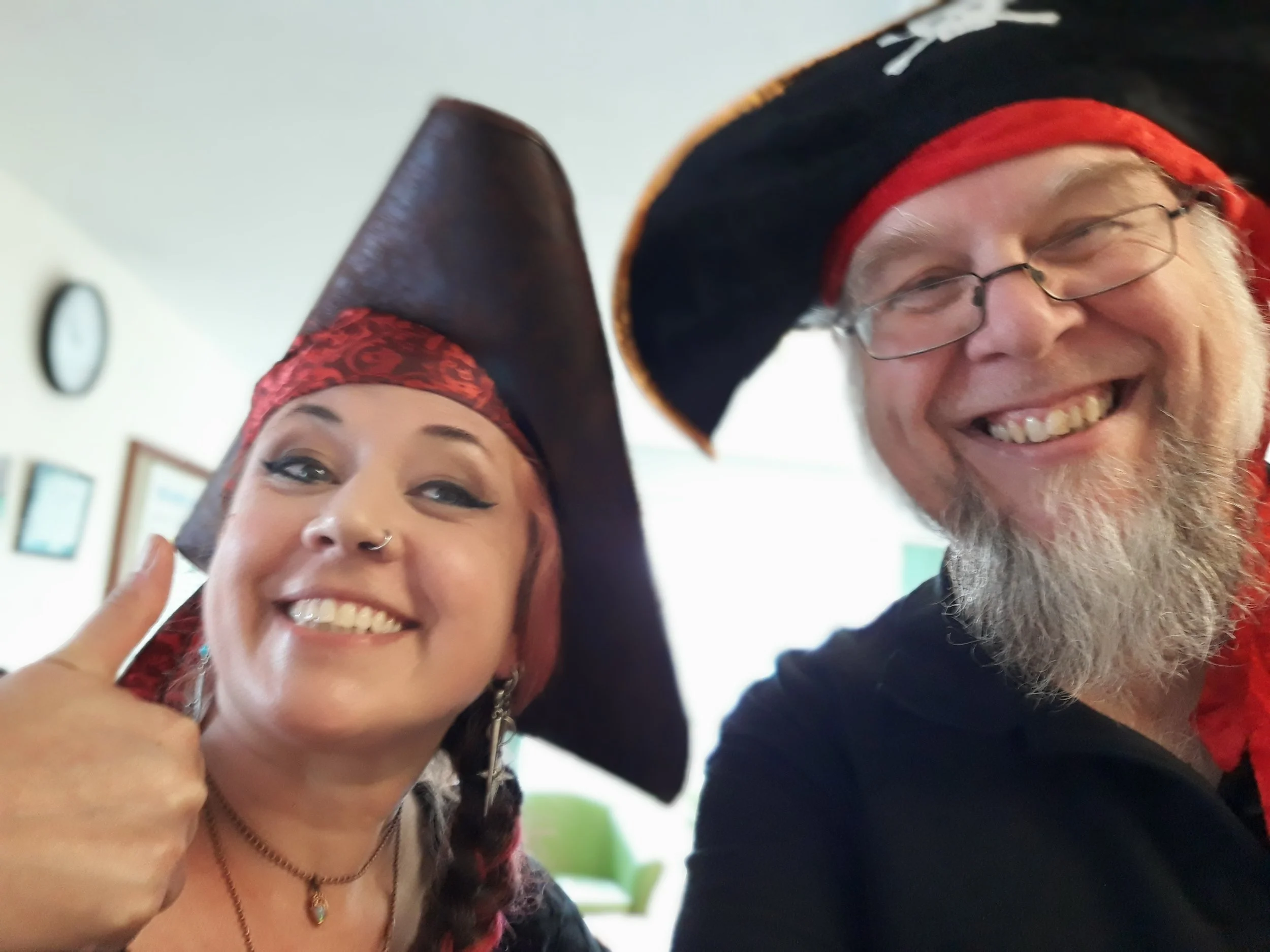 Two people smiling and wearing pirate hats, posing for a selfie indoors.