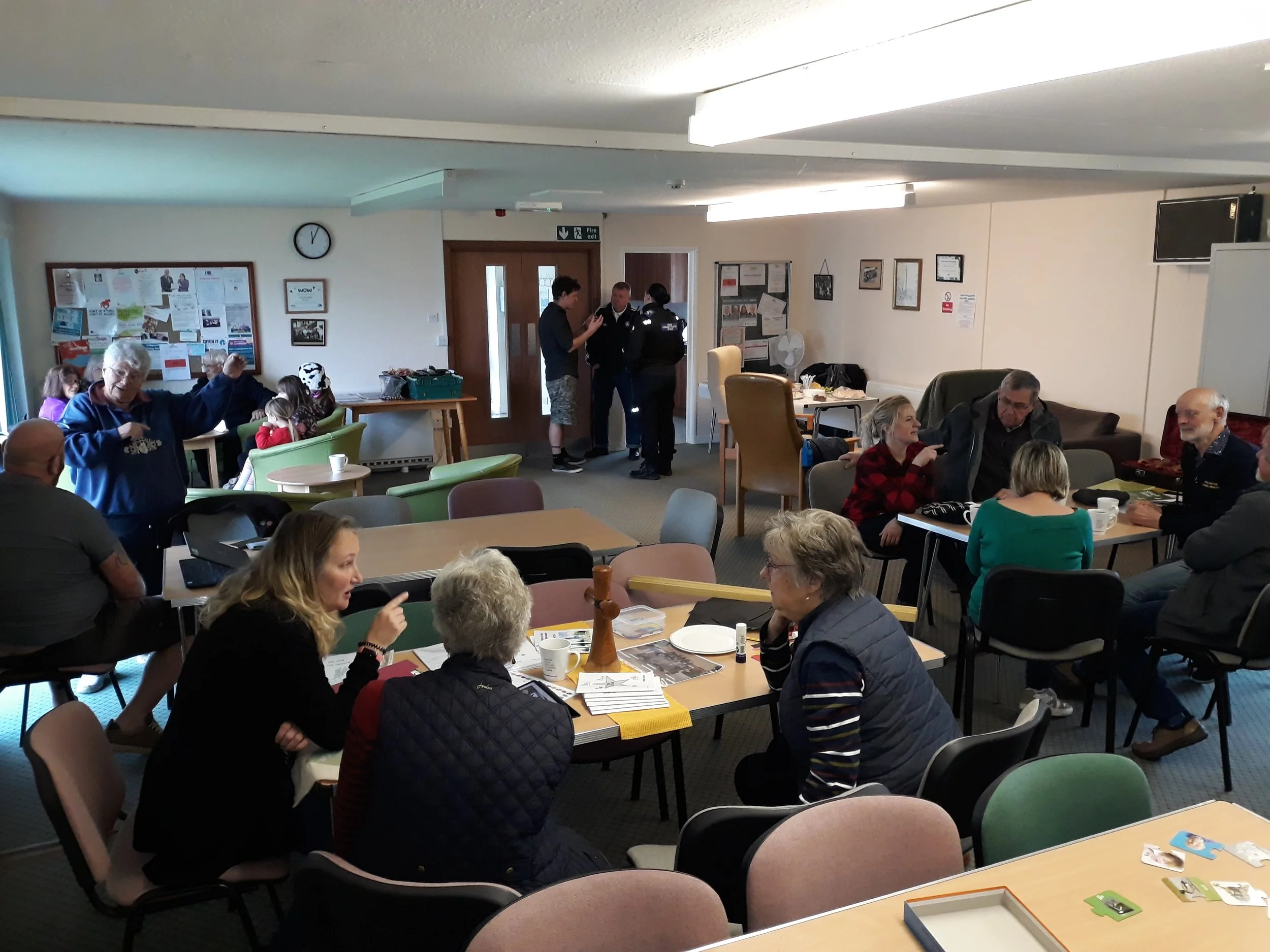 Two women sitting at a table, one holding community event flyer and the other with a laptop and notepad.