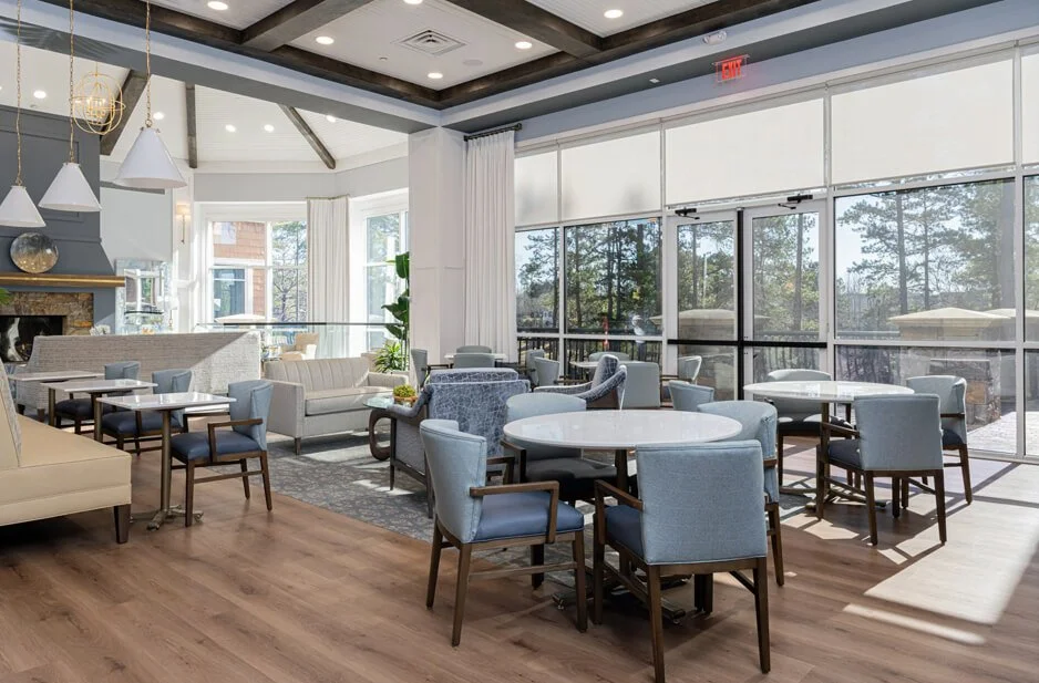 Bright, modern coffee cafe with round tables, upholstered chairs, large windows, and a mix of casual and formal seating.